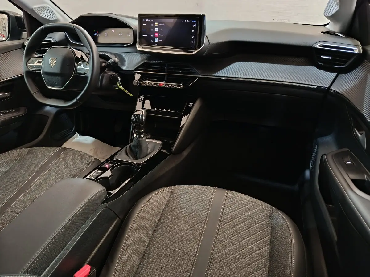 Intérieur de la Peugeot 208 PureTech 100 S&S Allure 2025 en gris, vue côté conducteur avec tableau de bord et boîte manuelle.