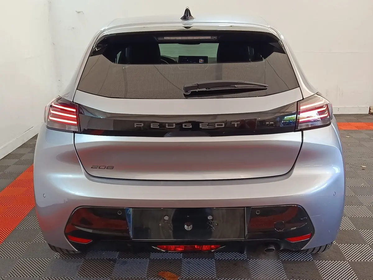 Vue arrière d'une Peugeot 208 gris clair 2025 avec feux LED et hayon fermé dans un garage.