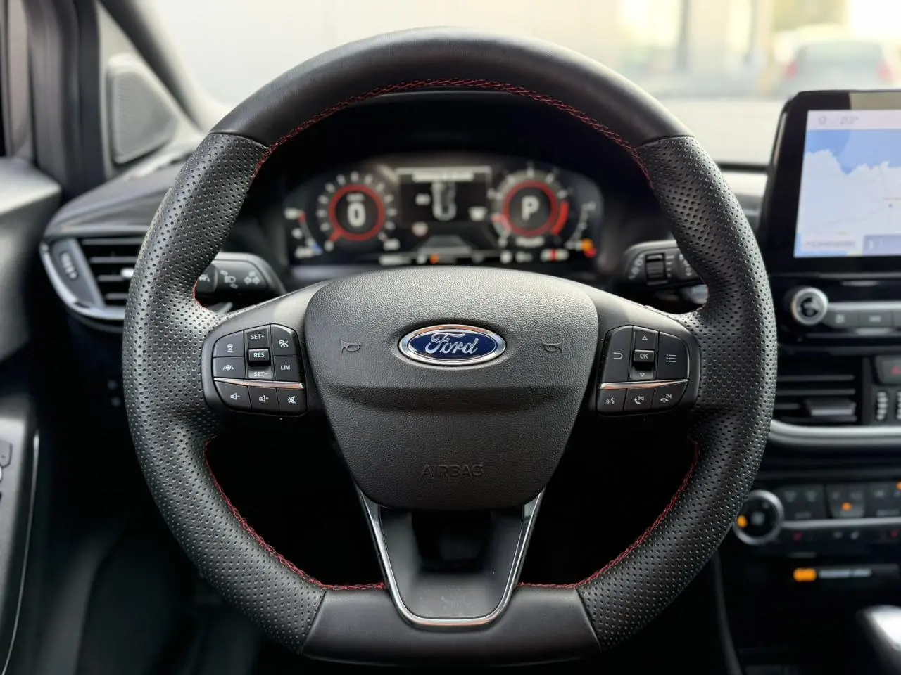 Gros plan sur le volant ST-Line en cuir perforé avec surpiqûres rouges du Ford Puma 2024, tableau de bord numérique et écran GPS visibles.