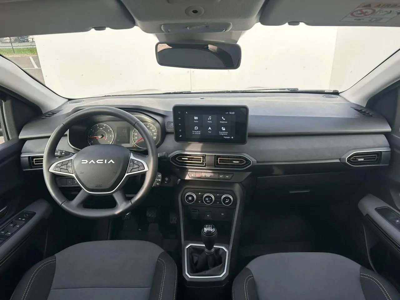 Vue intérieure avant du tableau de bord et volant de la Dacia Sandero III Stepway avec écran tactile et boîte manuelle.