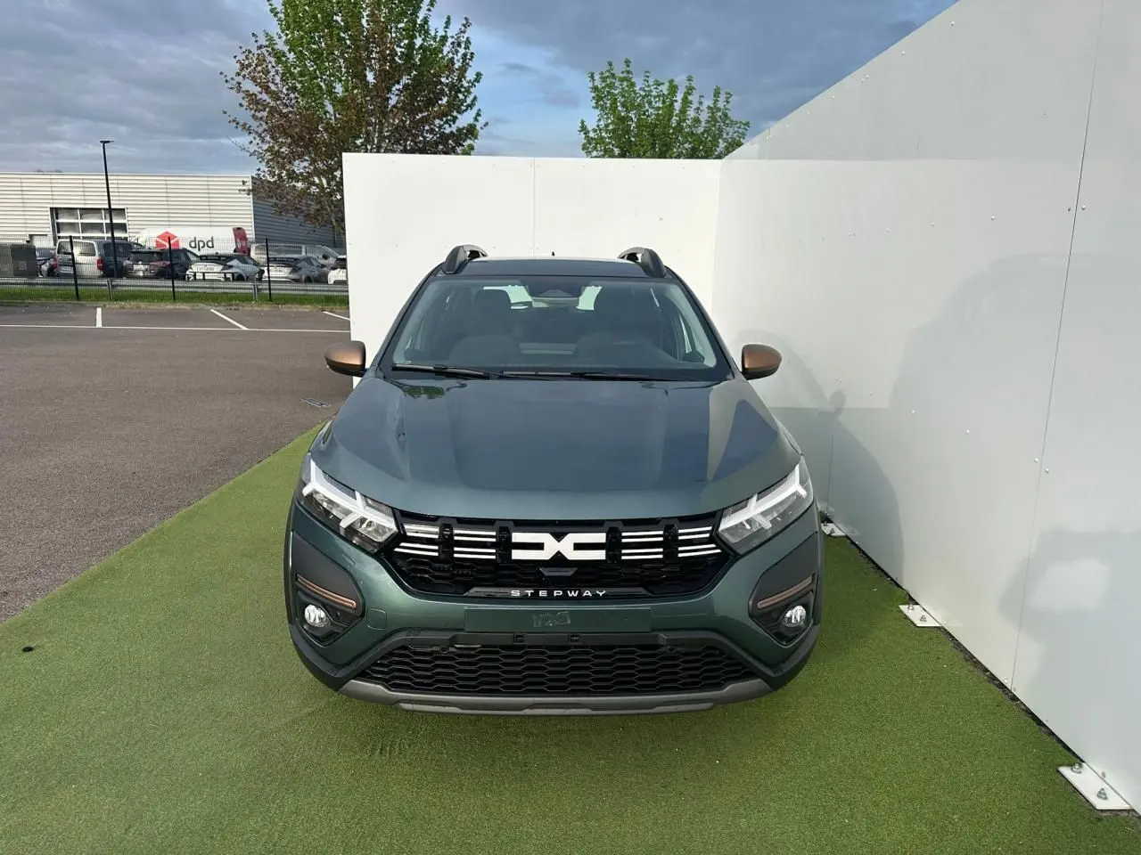 Vue avant frontale d'une Dacia Sandero III Stepway 2025 en vert cèdre avec calandre noire et barres de toit.