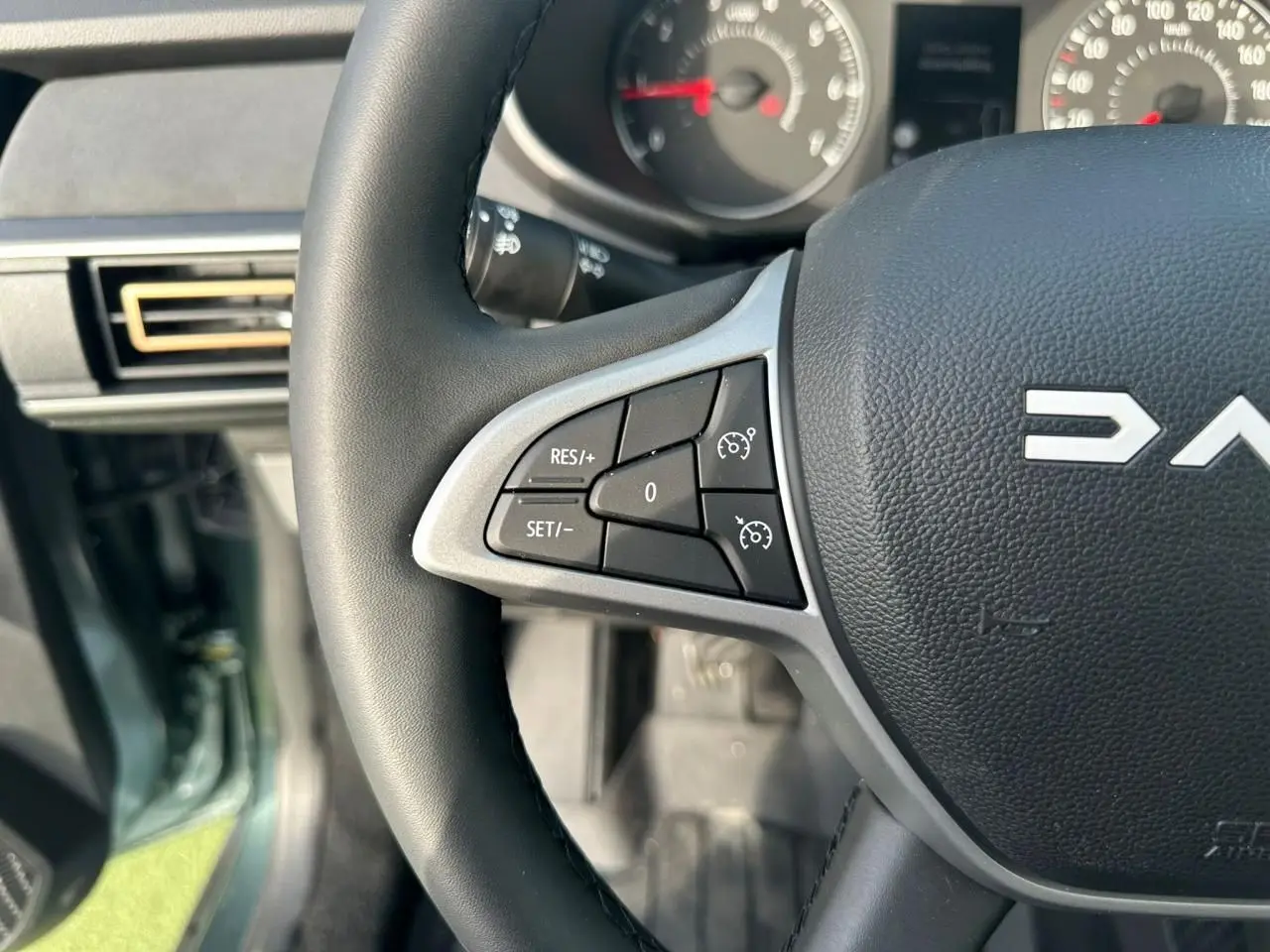 Gros plan sur le volant noir de la Dacia Sandero III Stepway avec commandes de régulateur de vitesse, intérieur gris.