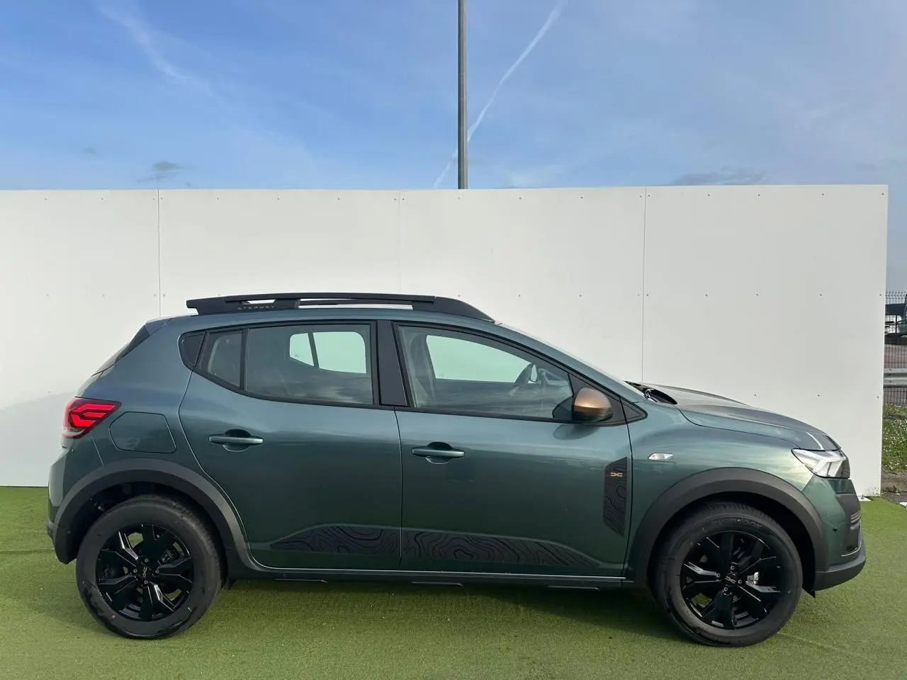 Profil droit de la Dacia Sandero III Stepway 2025 en Vert Cèdre avec jantes noires et barres de toit brun cuivré.