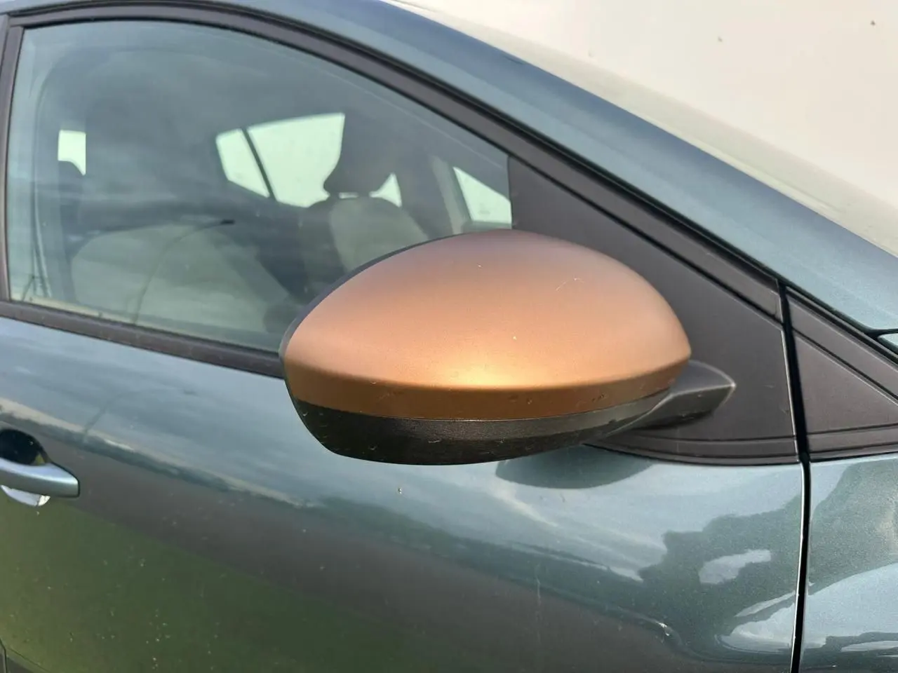 Gros plan sur le rétroviseur brun cuivré côté conducteur d'une Dacia Sandero III Stepway Vert Cèdre.