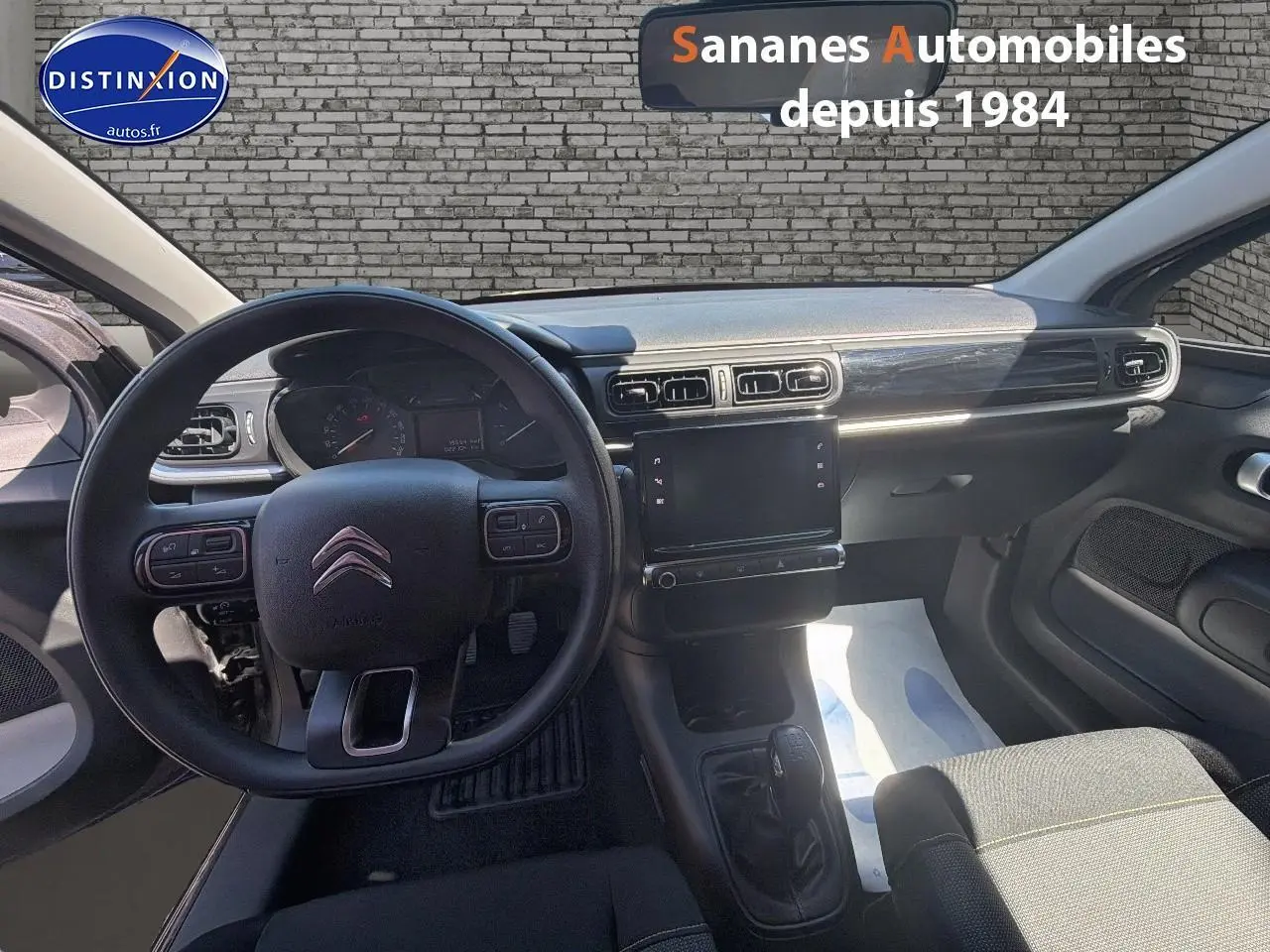 Vue intérieure avant centrée sur le volant et la console centrale d'une Citroën C3 2022 avec sellerie tissu gris.