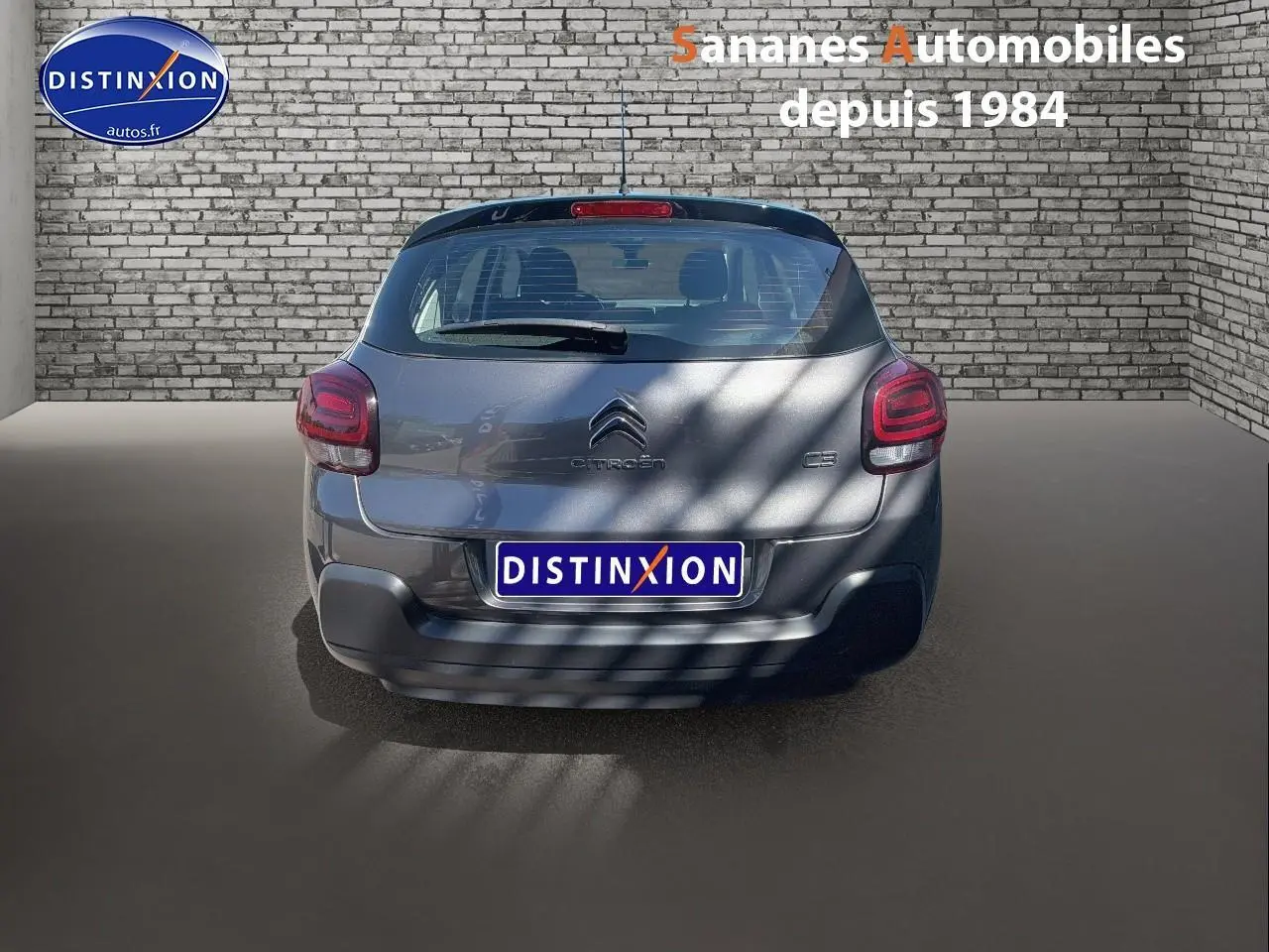 Vue arrière d'une Citroën C3 gris foncé 2022 avec feux arrière LED et logo centré sur fond brique.