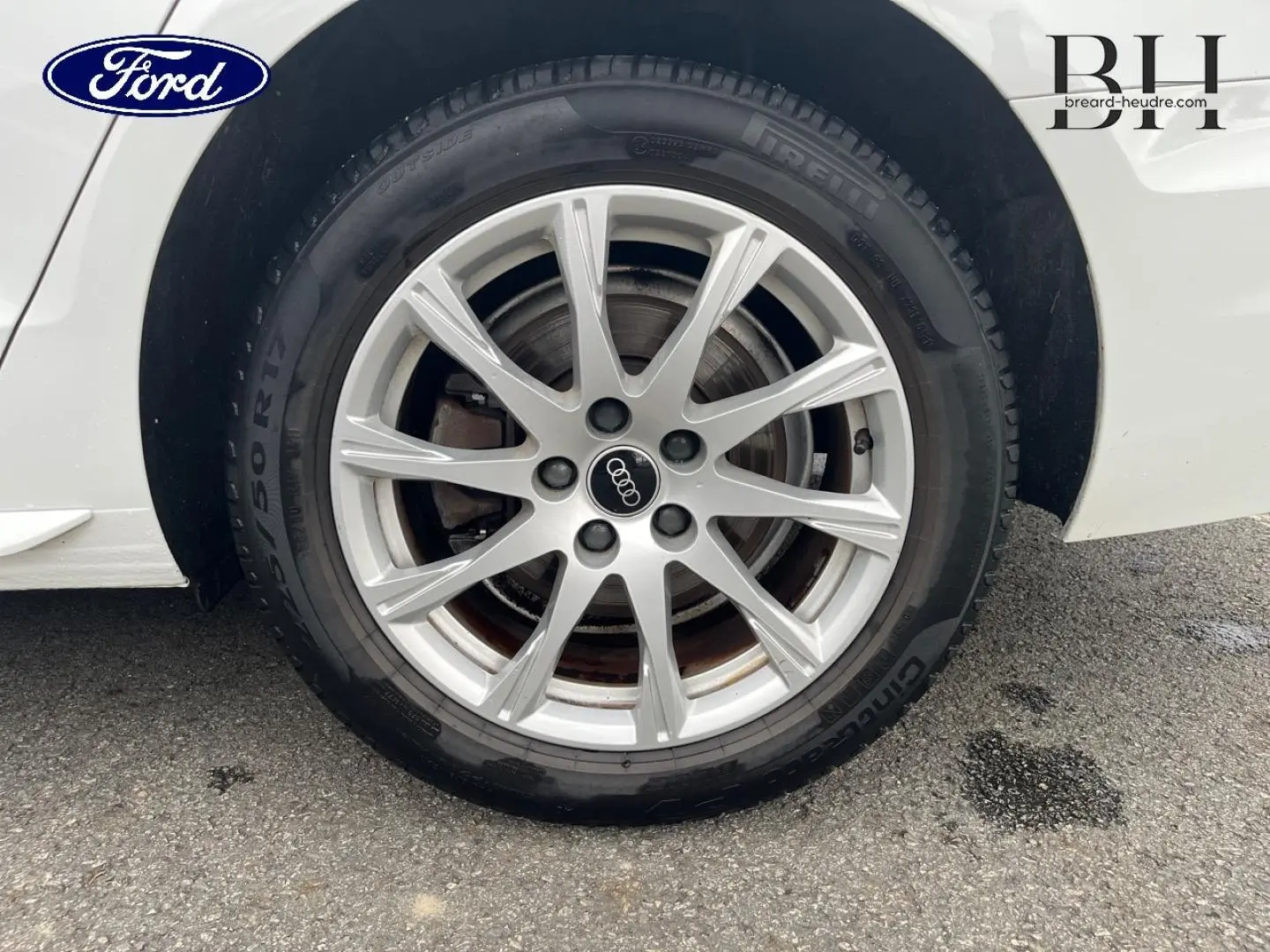 Gros plan sur la jante alu argentée avec logo Audi d'une roue arrière droite d'Audi A4 Avant blanc glacier métallisé.