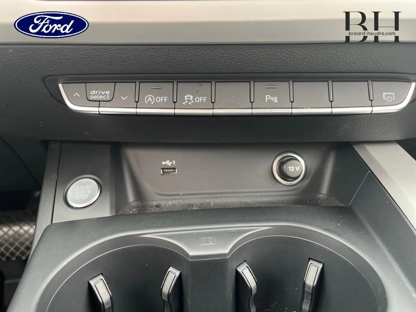 Vue rapprochée de la console centrale noire d'une Audi A4 Avant blanche, montrant les boutons de contrôle et prises USB et 12V.
