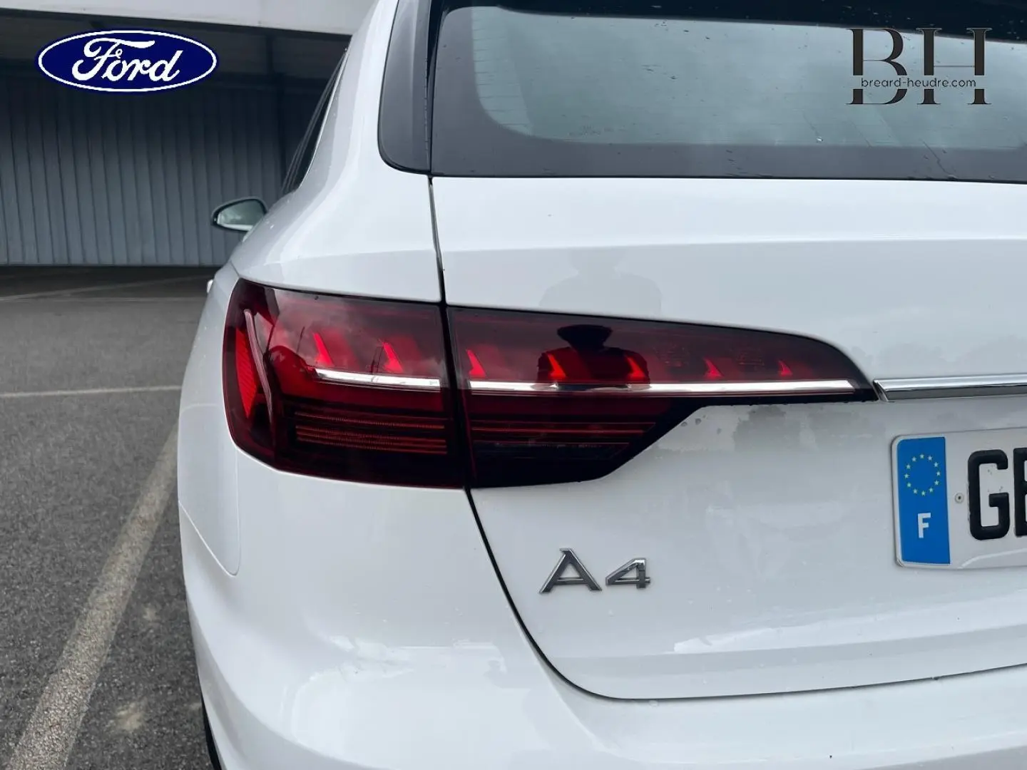 Vue arrière gauche d'une Audi A4 Avant blanc glacier métallisé avec feux arrière LED et logo A4 visible.