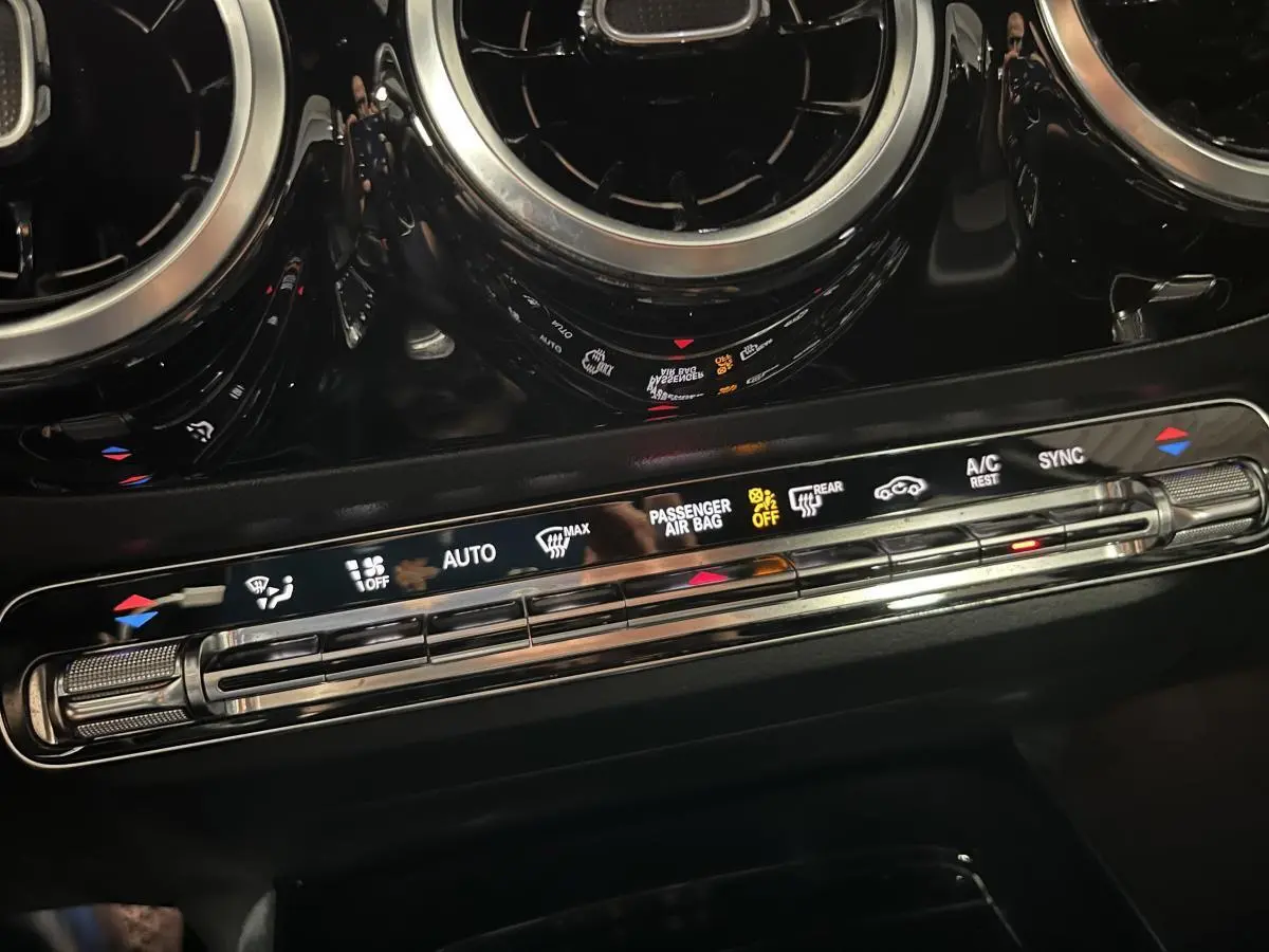 Détail de la console centrale noire du Mercedes Classe B 180 d 2019 avec commandes climatisation et aérateurs ronds chromés.