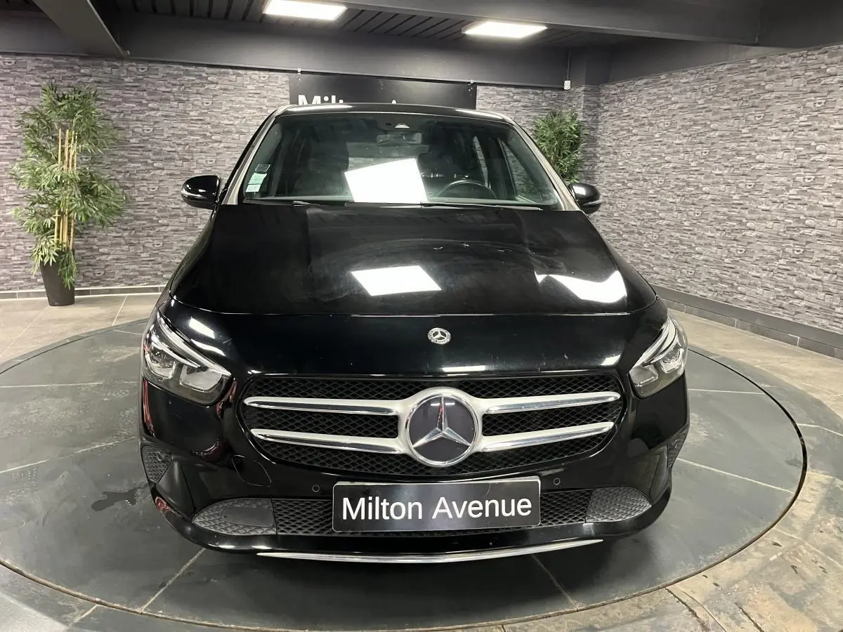 Vue avant d'une Mercedes Classe B noire avec calandre chromée et logo central, sur plateau tournant intérieur.