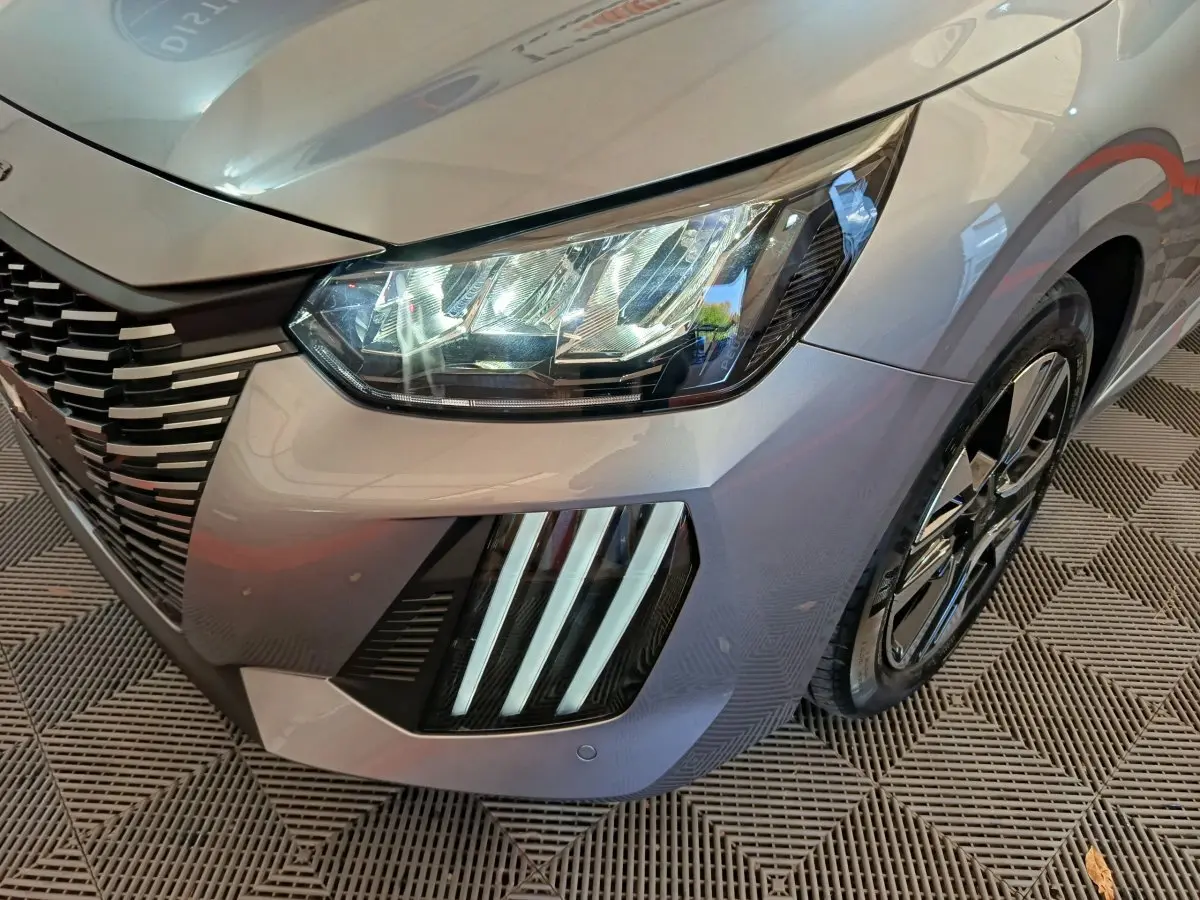 Gros plan sur l'avant droit gris clair de la Peugeot 208 2025 avec phares LED et signature lumineuse verticale distinctive.