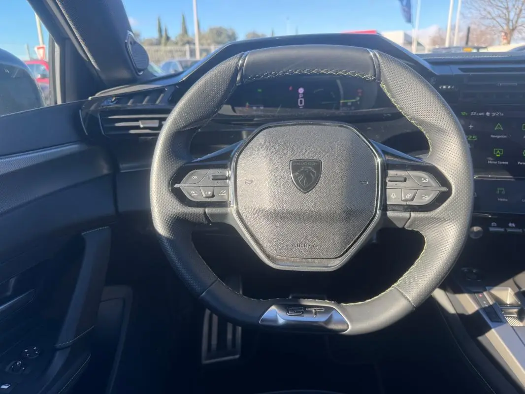 Vue rapprochée du volant cuir noir GT de la Peugeot 408 Hybrid 2024 avec commandes intégrées et cockpit numérique en arrière-plan.