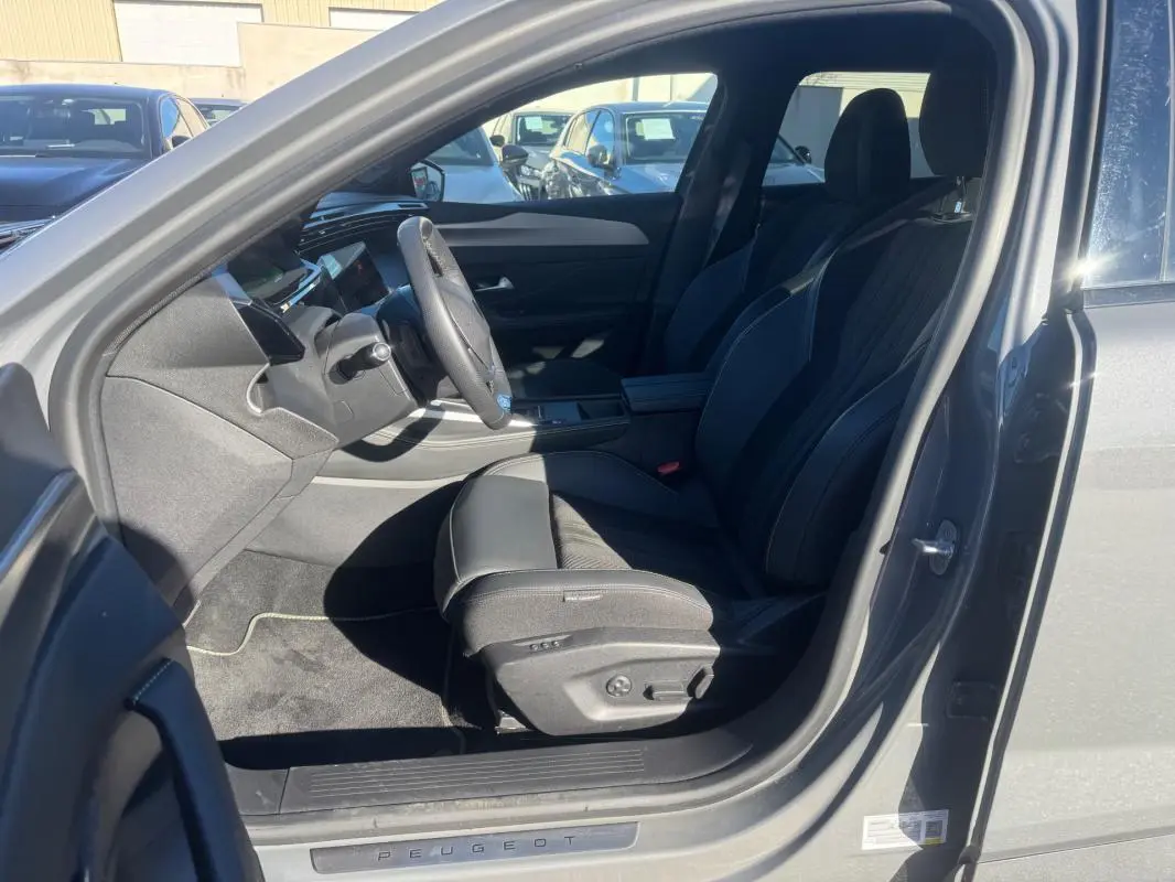 Vue intérieure côté conducteur de la Peugeot 408 Hybrid gris 2024, sièges cuir noirs et volant cuir multifonction.