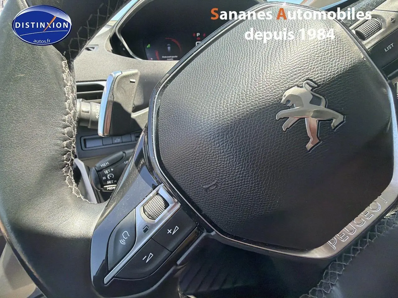 Gros plan sur le volant cuir noir du Peugeot 3008 avec commandes intégrées et logo lion argenté au centre.
