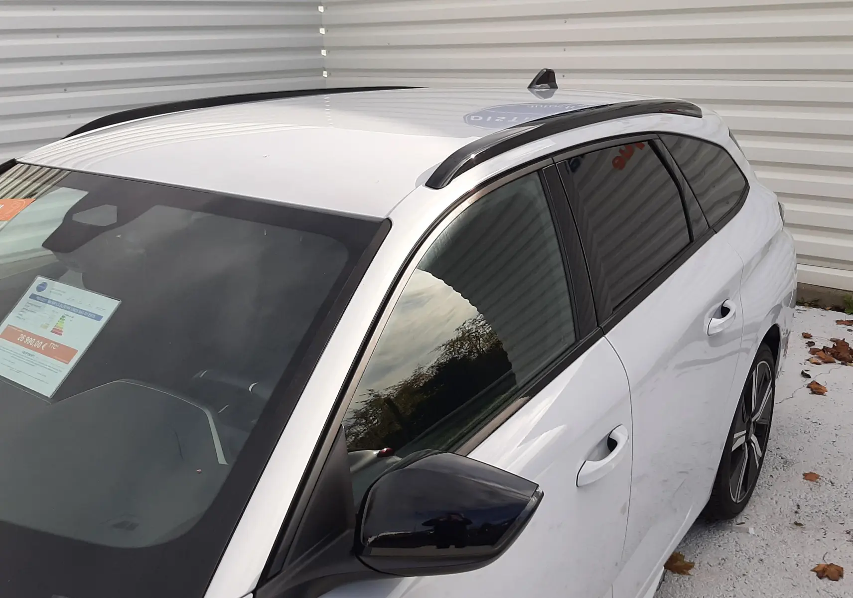 Vue 3/4 avant droit d’une Peugeot 308 SW 2024 blanc okenite avec toit noir et barres de toit noires.