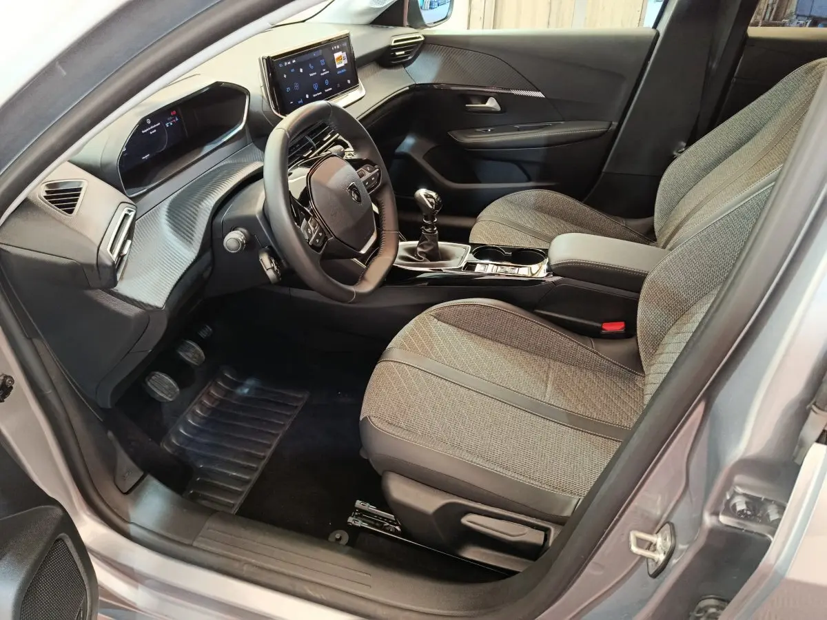 Intérieur avant droit de la Peugeot 208 gris clair 2025, volant cuir, écran tactile et sièges tissu gris.