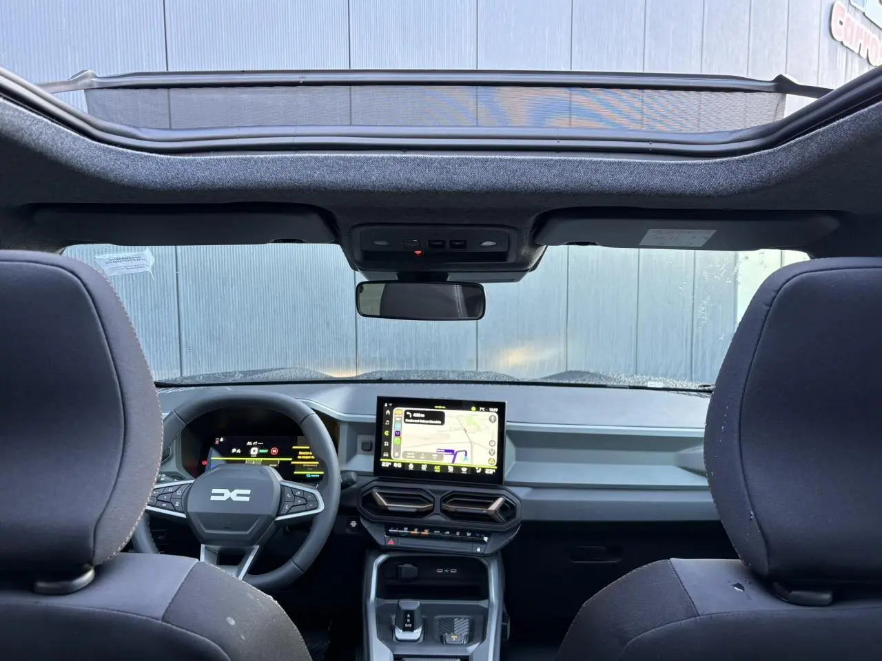 Vue intérieure avant du Dacia Bigster 2026 noir nacré, avec tableau de bord numérique et toit panoramique ouvert.