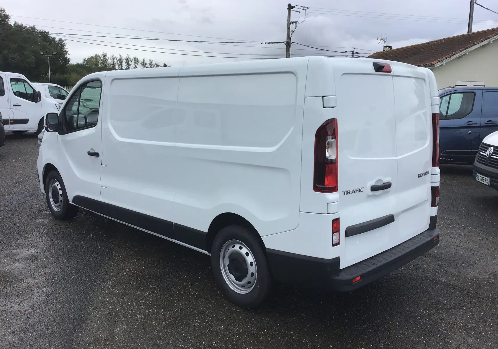 Renault Trafic Fourgon blanc en vue 3/4 arrière droit, avec caméra de recul et feux arrière verticaux visibles.