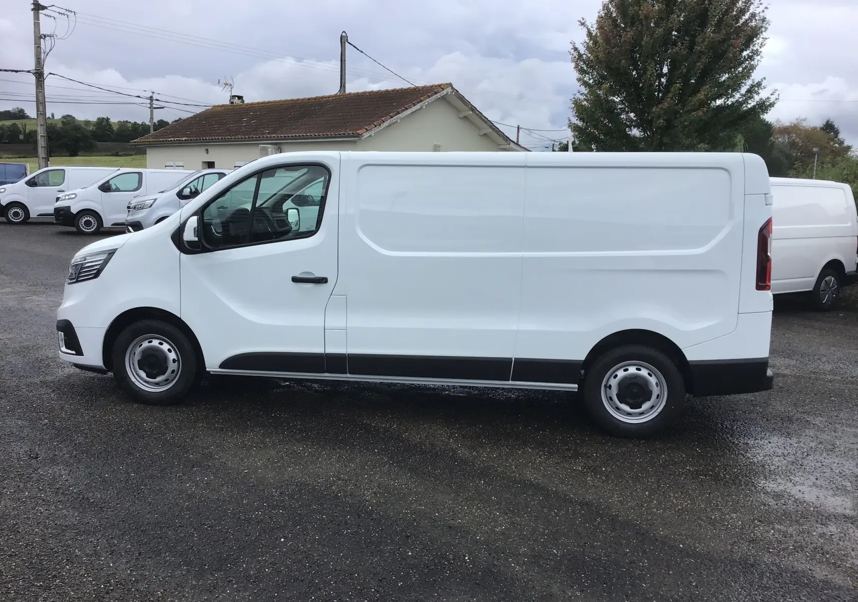 Renault Trafic Fourgon blanc vu de profil côté gauche, avec porte latérale coulissante et jantes acier simples.