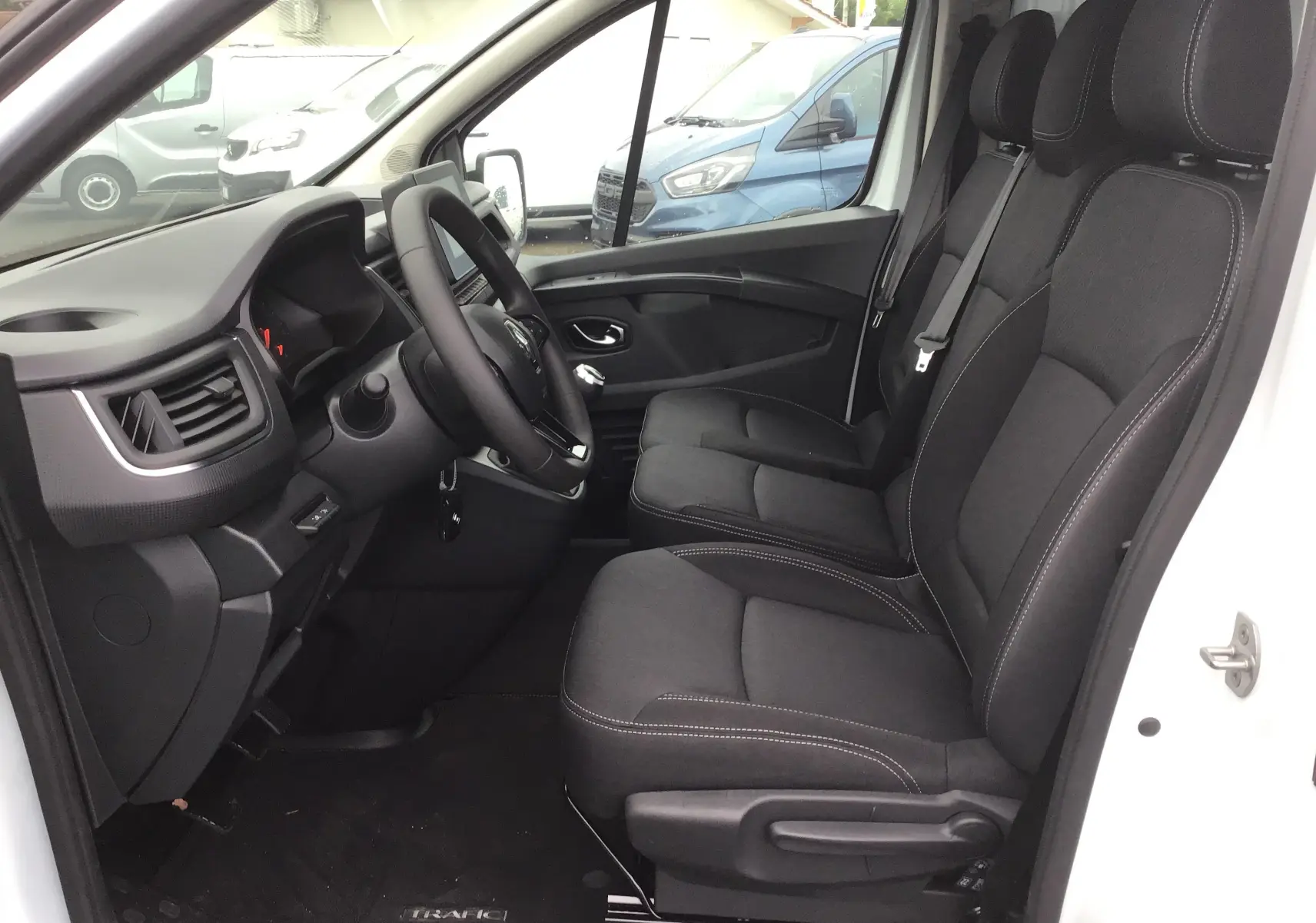 Intérieur côté conducteur du Renault Trafic Fourgon blanc 2023, sièges noirs et tableau de bord moderne visible.