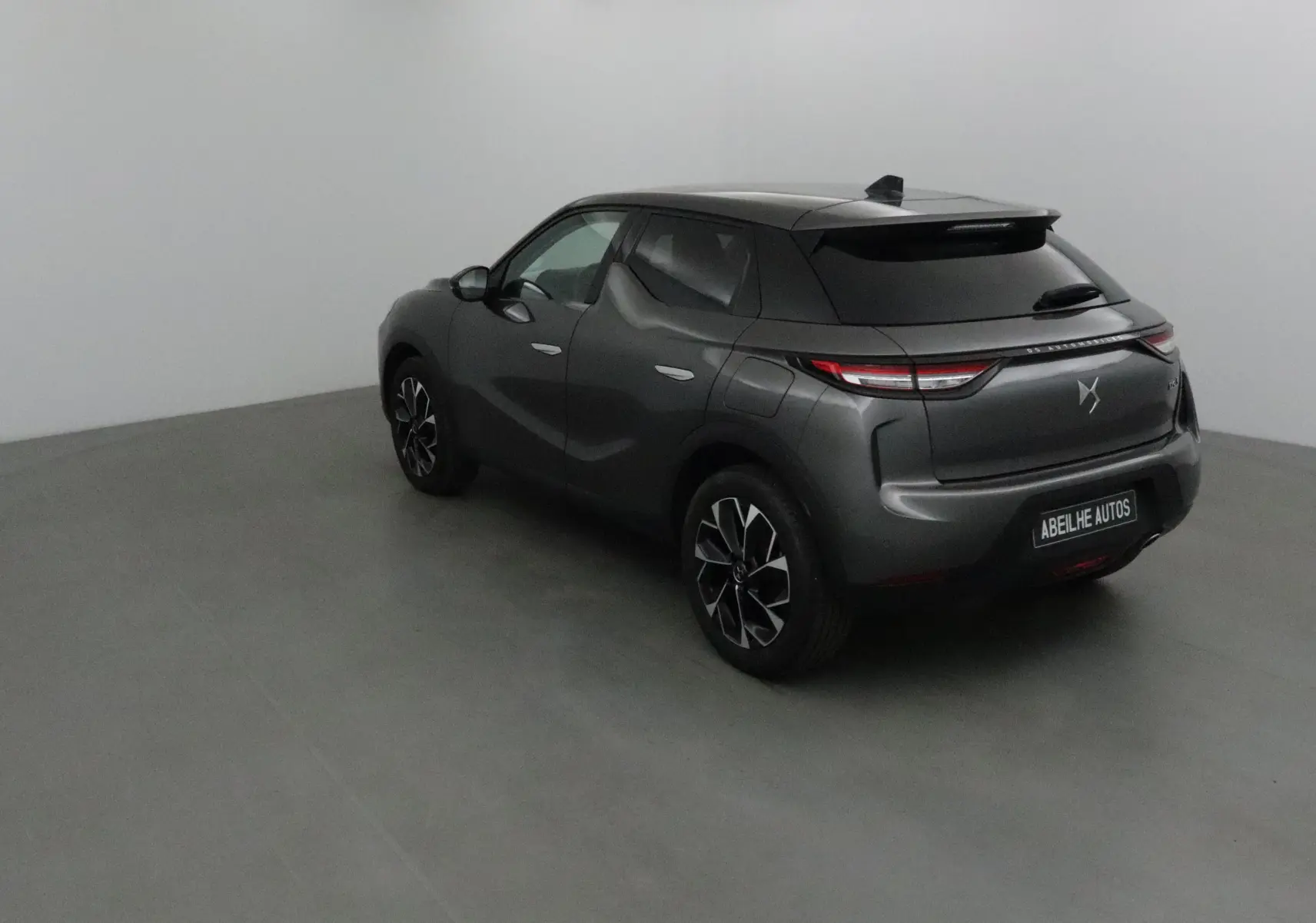 Vue 3/4 arrière droite d'un DS3 Crossback gris platinium avec jantes noires et feux arrière LED allumés.
