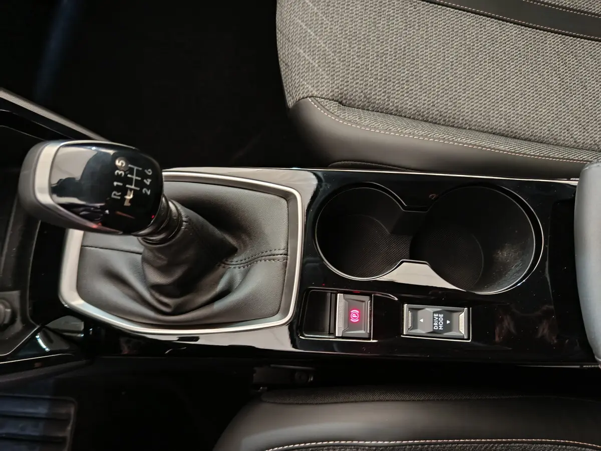 Vue rapprochée de la console centrale noire avec levier de vitesse manuel et porte-gobelets dans une Peugeot 208 gris clair.