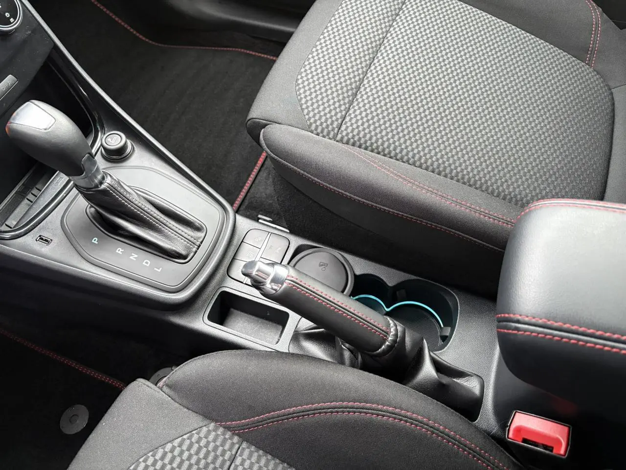 Vue rapprochée de la console centrale du Ford Puma 2024, sièges noirs avec surpiqûres rouges et levier de vitesse automatique.