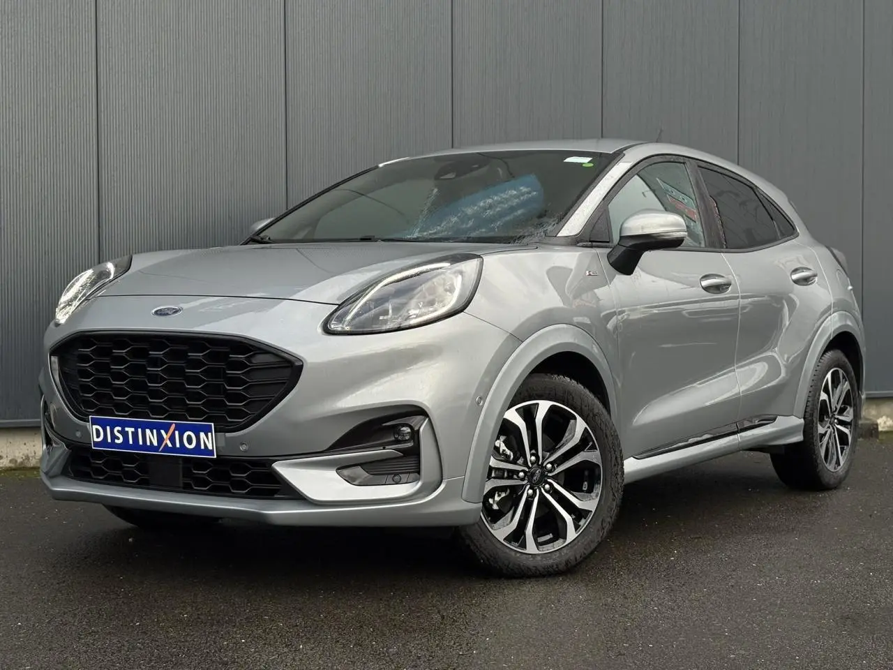 Ford Puma Ecoboost gris Solar en vue 3/4 avant droit, avec jantes alliage noires et calandre noire distinctive.