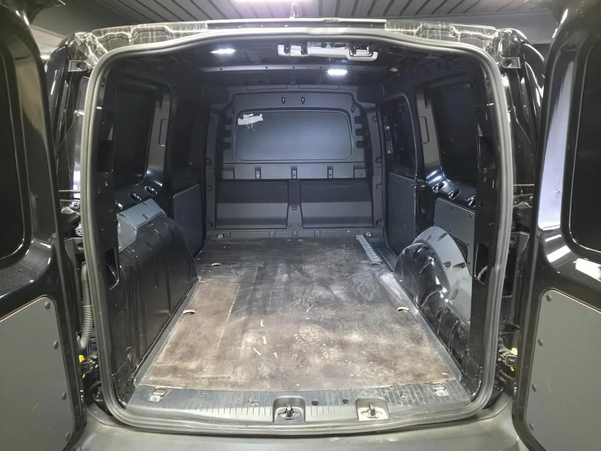 Vue arrière ouverte du coffre noir du Volkswagen Caddy Cargo 2024, montrant l'espace de chargement vide avec revêtement caoutchouc.