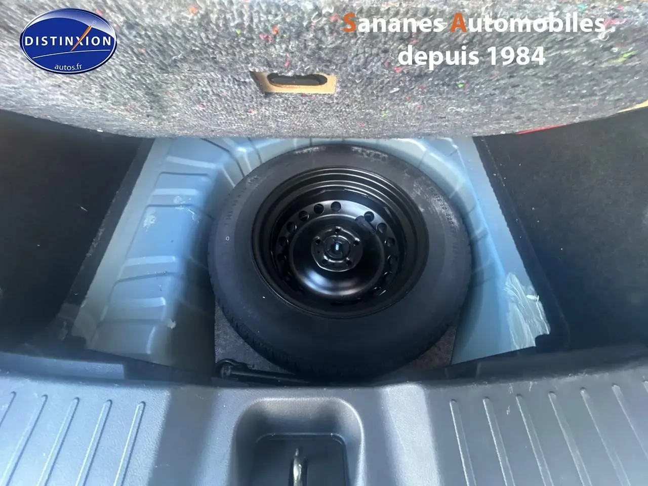 Vue plongeante sur la roue de secours noire dans le coffre d'un Nissan Juke bleu clair 2020.