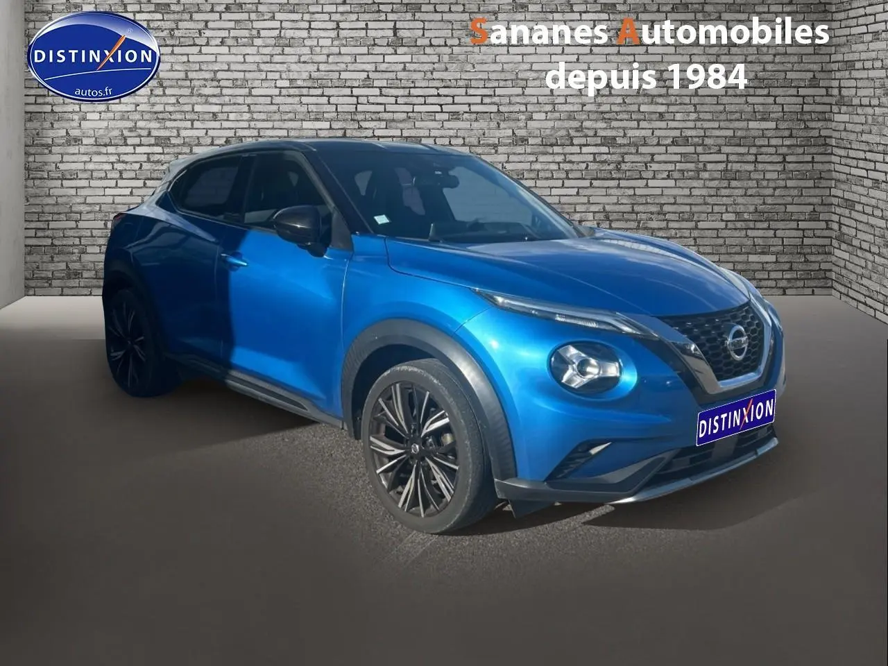 Nissan Juke bleu clair en 3/4 avant droit, avec jantes noires et calandre distinctive V-Motion.