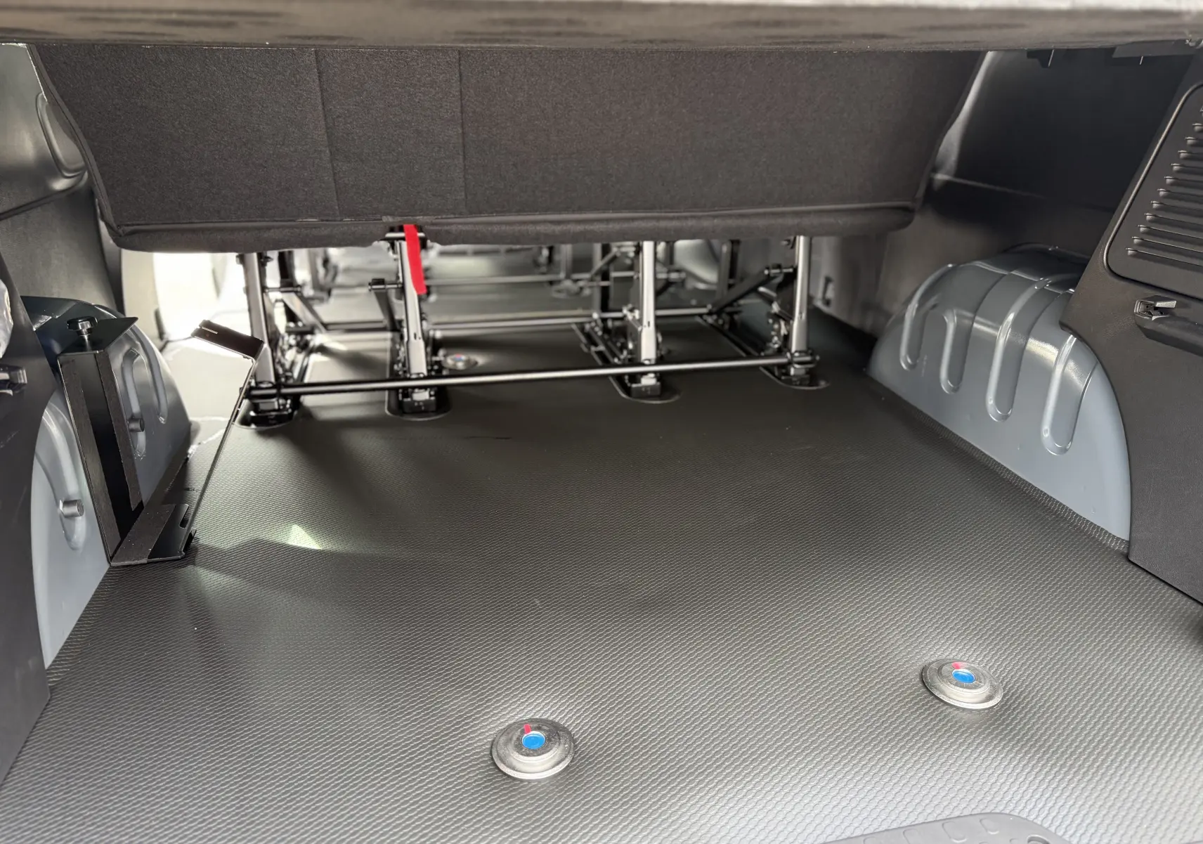 Vue intérieure du coffre du Renault Trafic Combi gris Urban 2025, montrant les fixations pour fauteuil roulant et la structure des sièges.