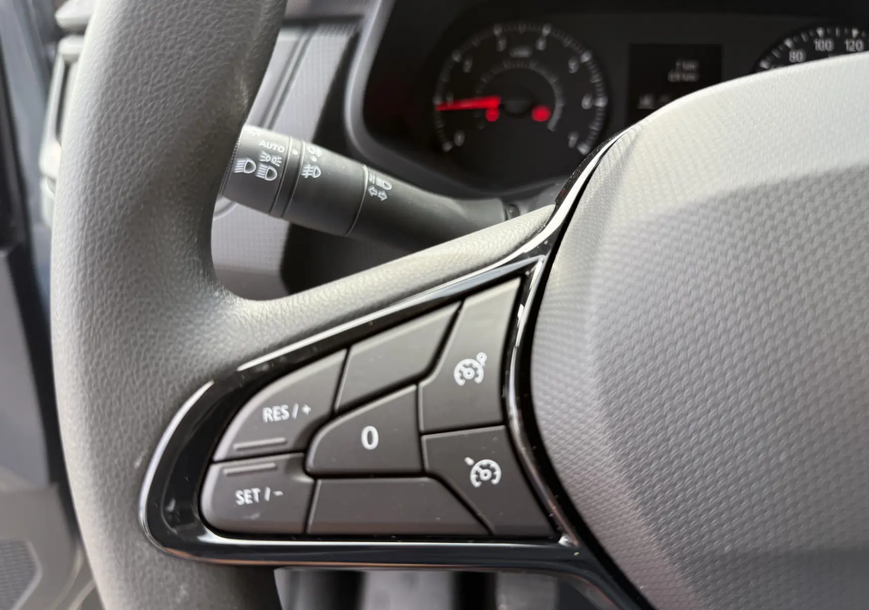Gros plan sur les commandes de régulateur de vitesse au volant gris du Renault Trafic Combi 2025, tableau de bord en arrière-plan.