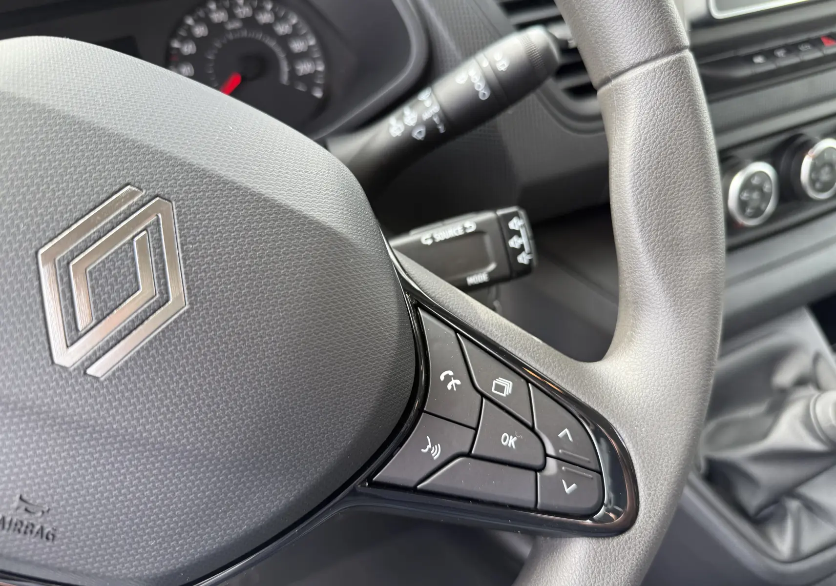 Gros plan sur le volant gris du Renault Trafic Combi 2025, avec commandes multifonctions et levier de vitesses manuel visible.