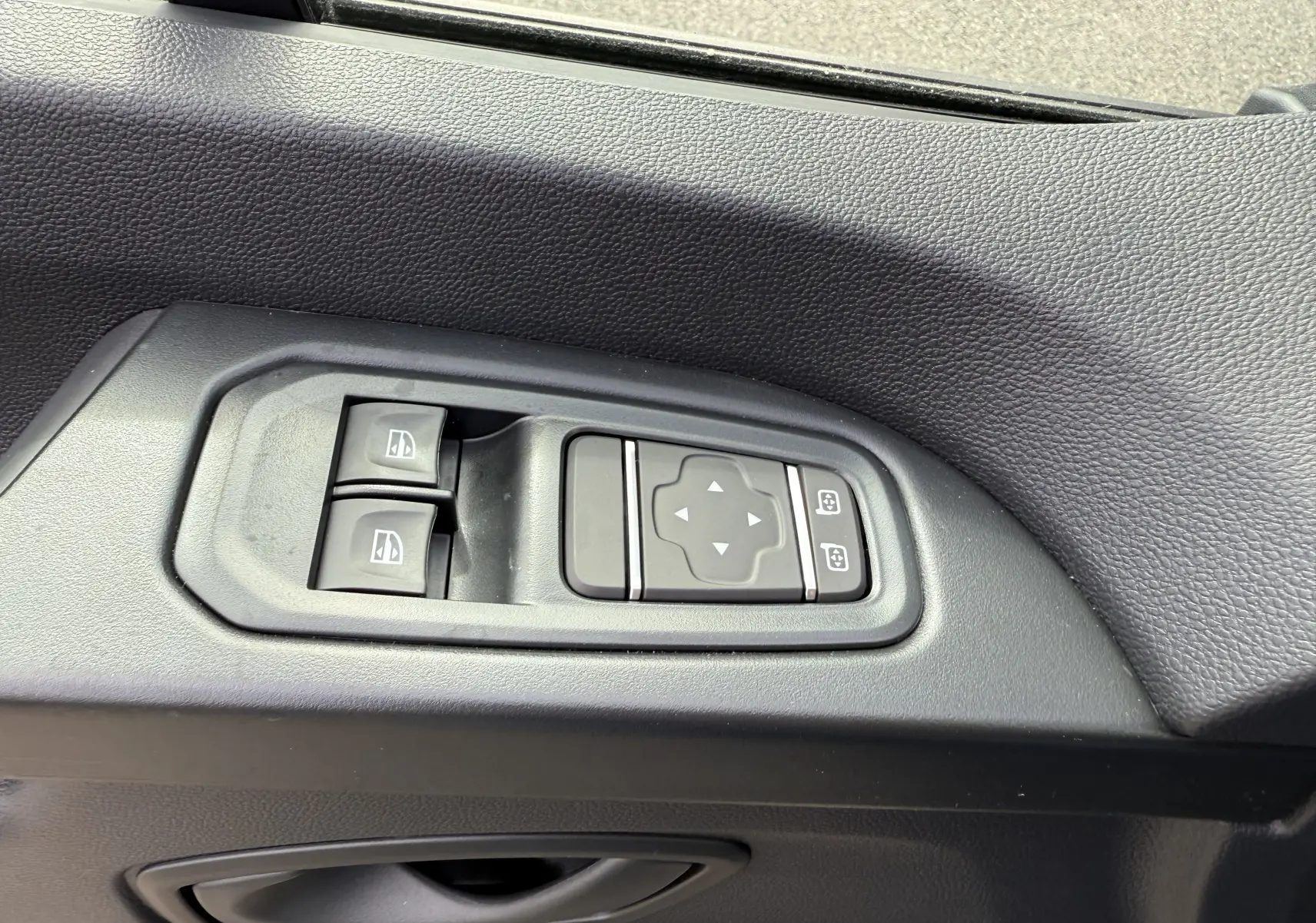 Gros plan sur les commandes électriques des vitres et des rétroviseurs côté conducteur du Renault Trafic Combi gris Urban 2025.