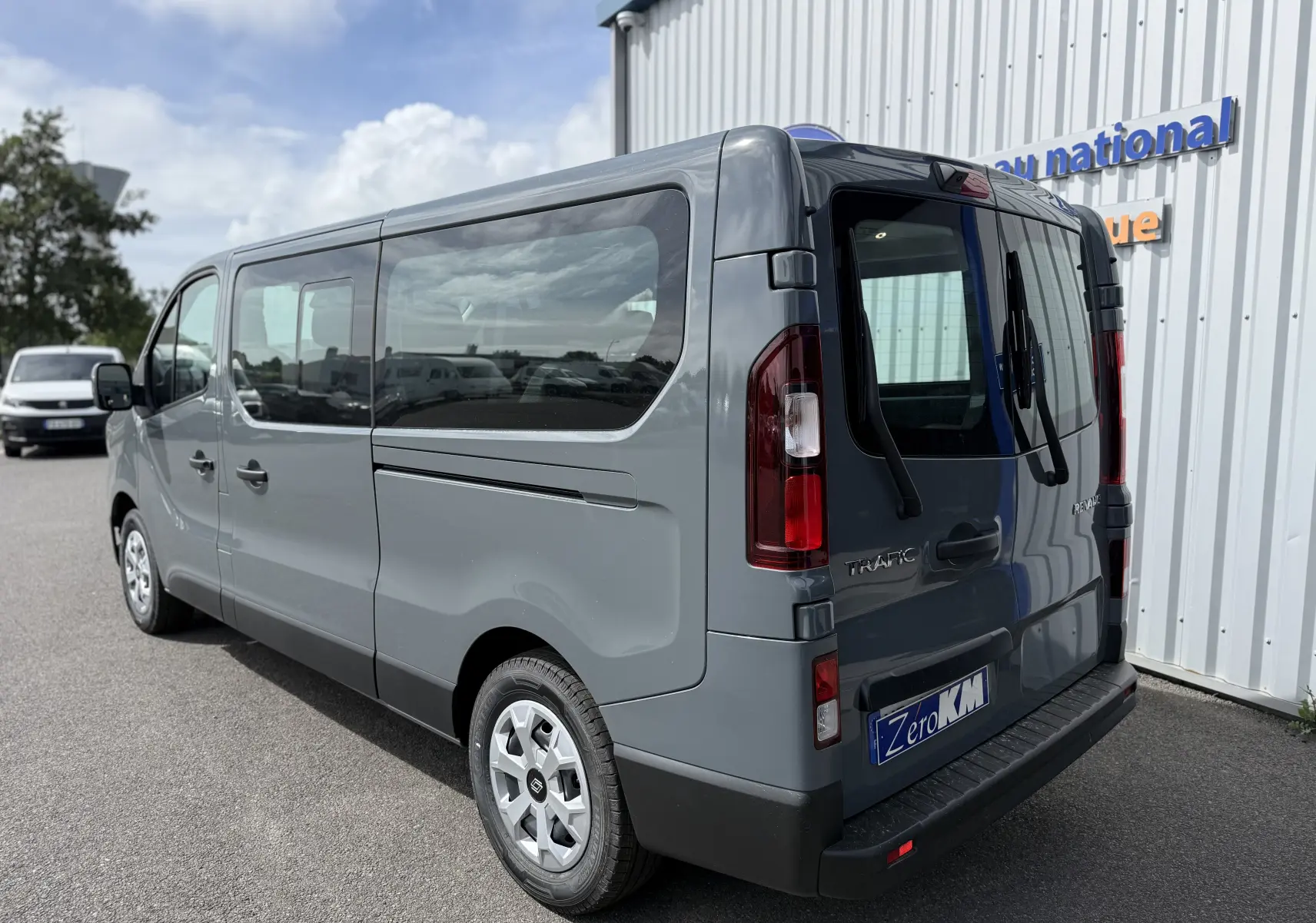 Vue 3/4 arrière droite d'un Renault Trafic Combi gris Urban 2025 avec vitres teintées et porte arrière vitrée.