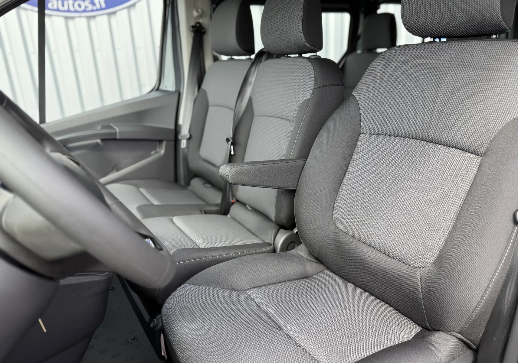 Vue intérieure côté conducteur du Renault Trafic Combi 2025, sièges tissu gris avec accoudoir central.