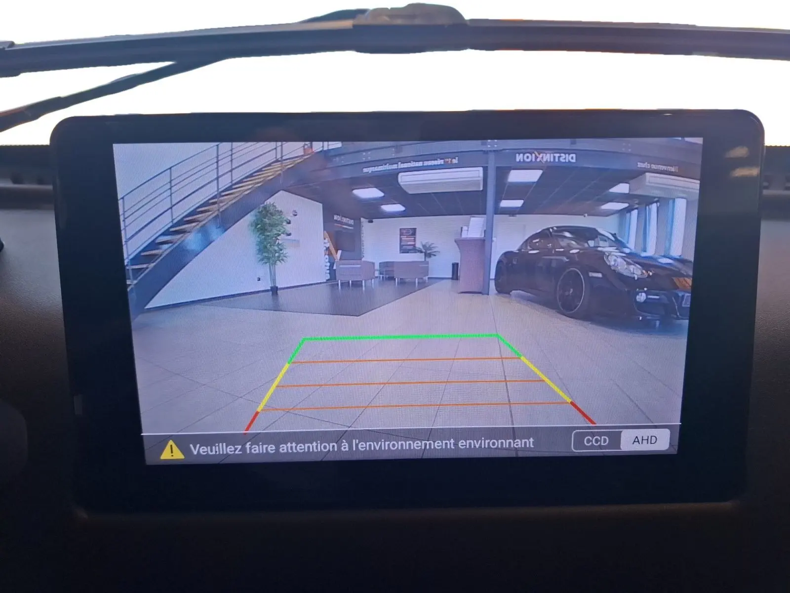 Écran de caméra de recul montrant un intérieur de garage avec une voiture noire stationnée à droite.