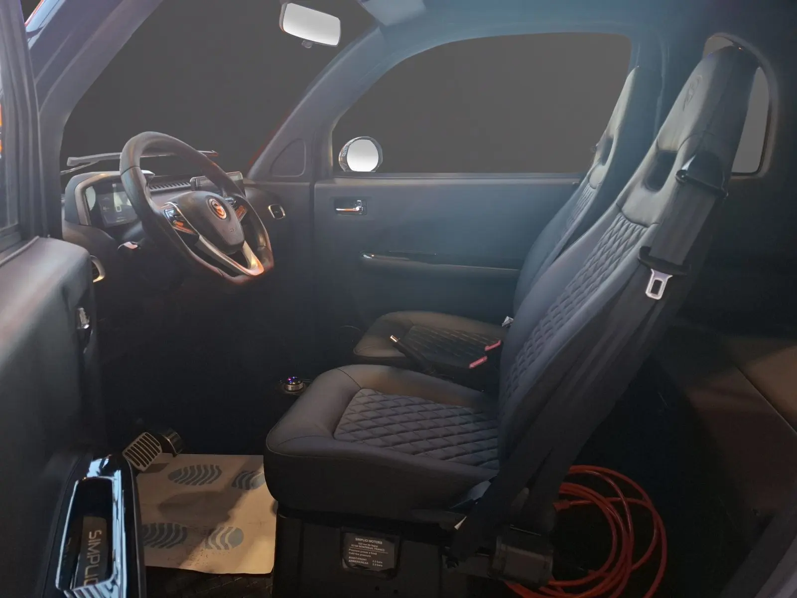 Vue intérieure côté conducteur de la SIMPLICI S1 2025 avec sièges noirs matelassés et volant multifonction.