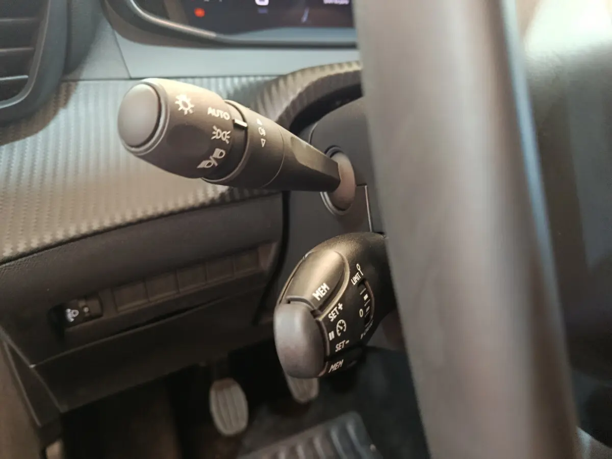 Gros plan sur les commandes au volant côté gauche de la Peugeot 208 gris foncé, montrant les fonctions de régulateur et éclairage.
