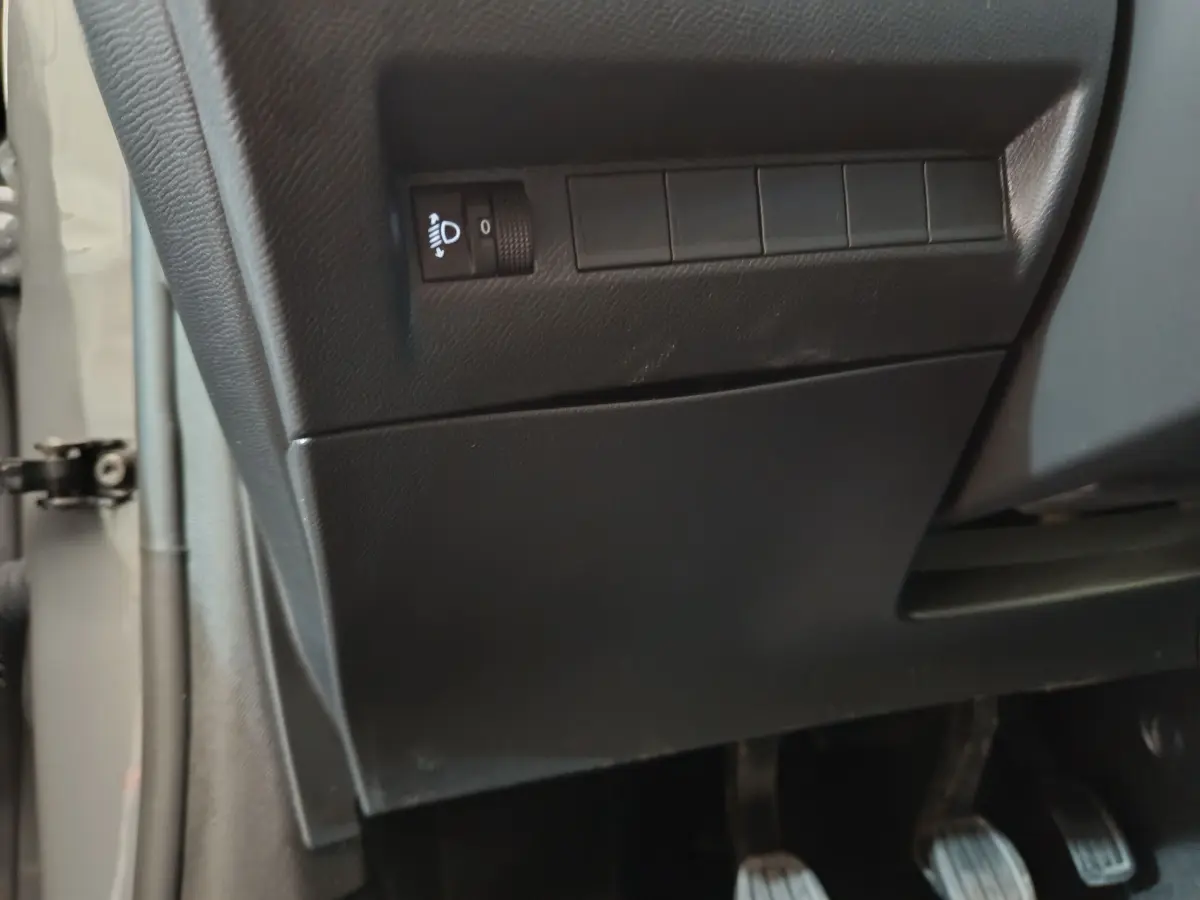 Détail du tableau de bord côté gauche en plastique noir avec commande de réglage des phares sur Peugeot 208 gris foncé.