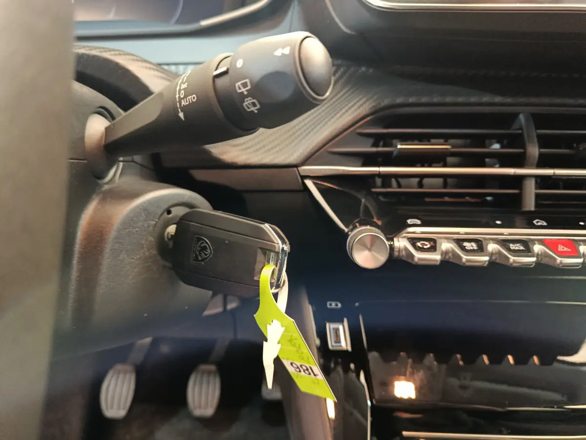 Gros plan sur le tableau de bord noir et la clé insérée dans le contacteur d'une Peugeot 208 gris foncé, version PureTech 100 S&S Allure.