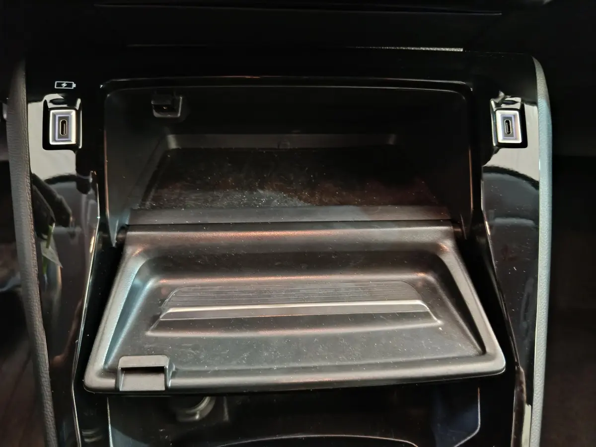 Vue rapprochée du rangement central ouvert avec ports USB dans l’habitacle noir brillant de la Peugeot 208 2025 gris foncé.
