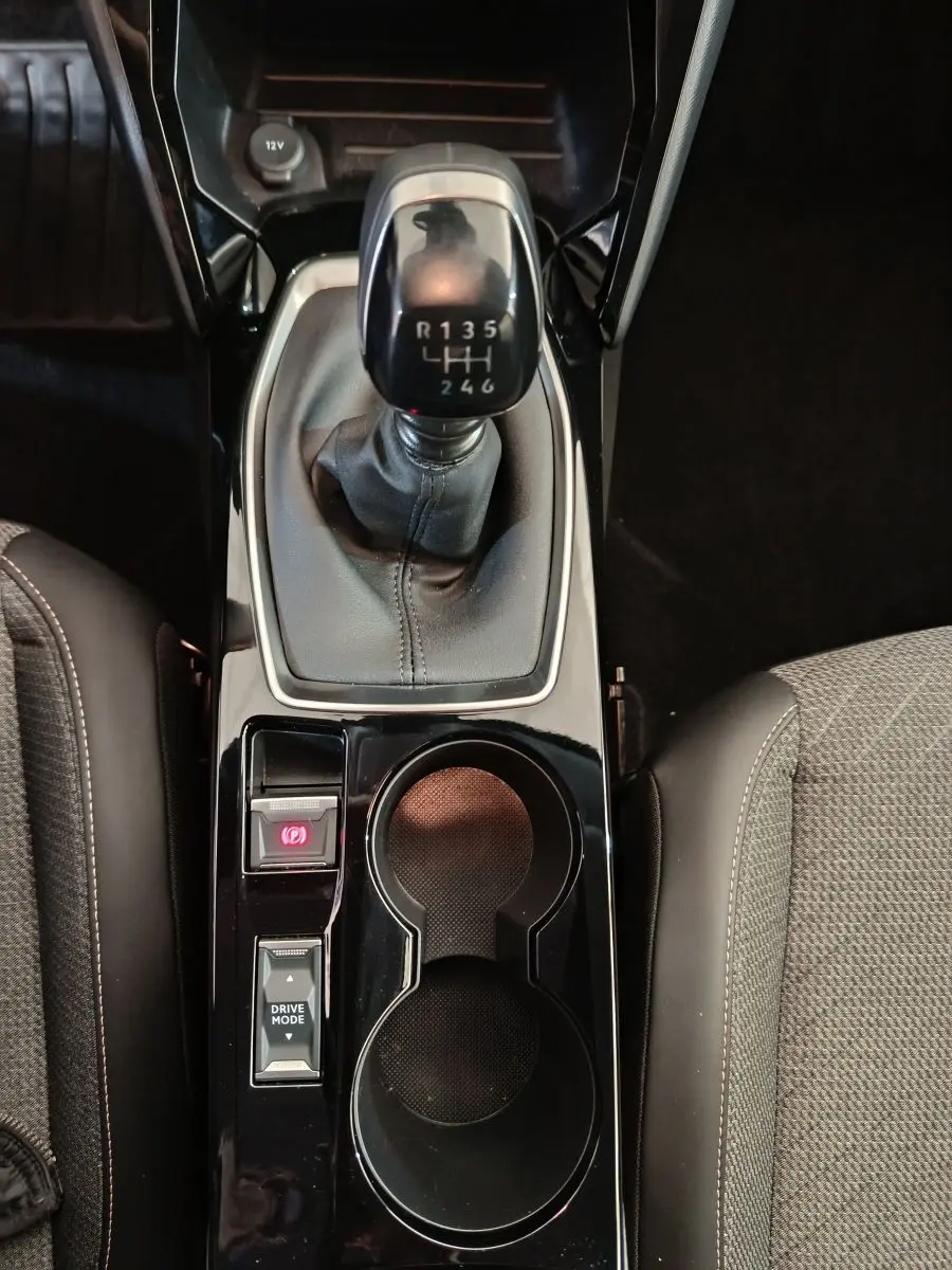 Vue plongeante sur la console centrale noire de la Peugeot 208 gris foncé avec levier de vitesse manuel et porte-gobelets.