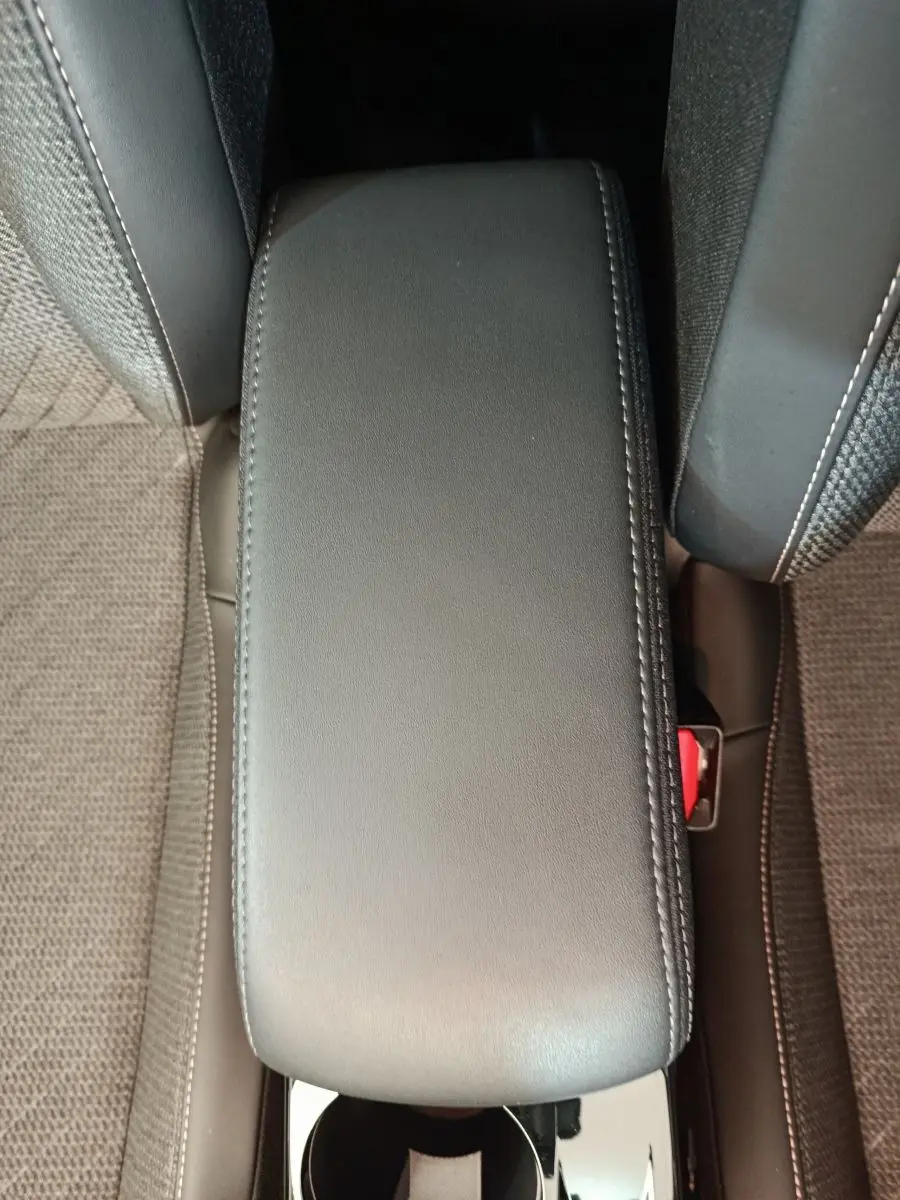 Accoudoir central avant en cuir gris foncé entre les sièges tissu de la Peugeot 208 PureTech 100 S&S Allure 2025.