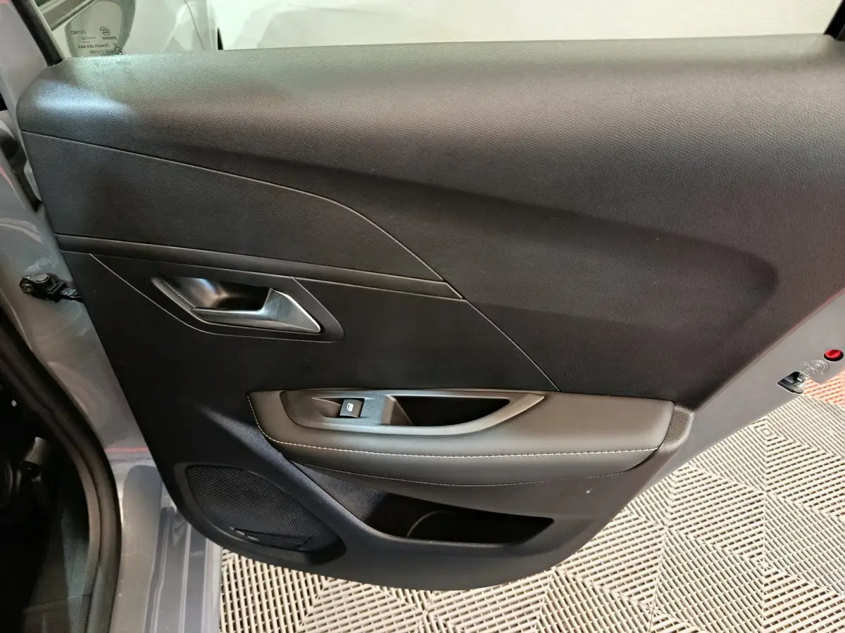 Vue rapprochée de la porte côté gauche gris foncé de la Peugeot 208 PureTech 100 S&S Allure avec poignée et commande de vitre.