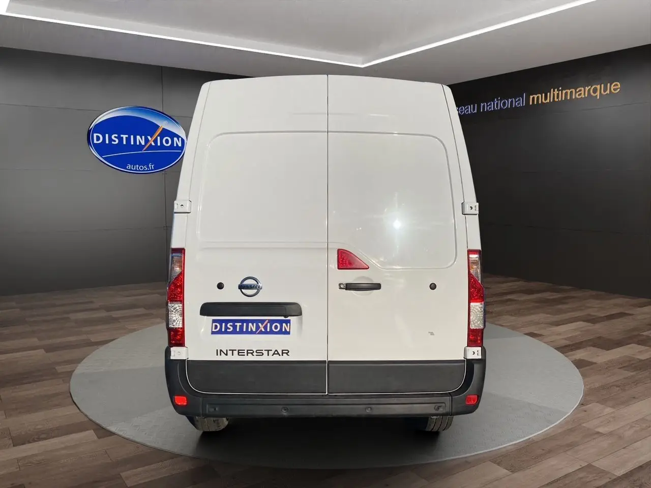 Vue arrière d’un utilitaire blanc Nissan Interstar avec portes battantes et logo visible en intérieur showroom.