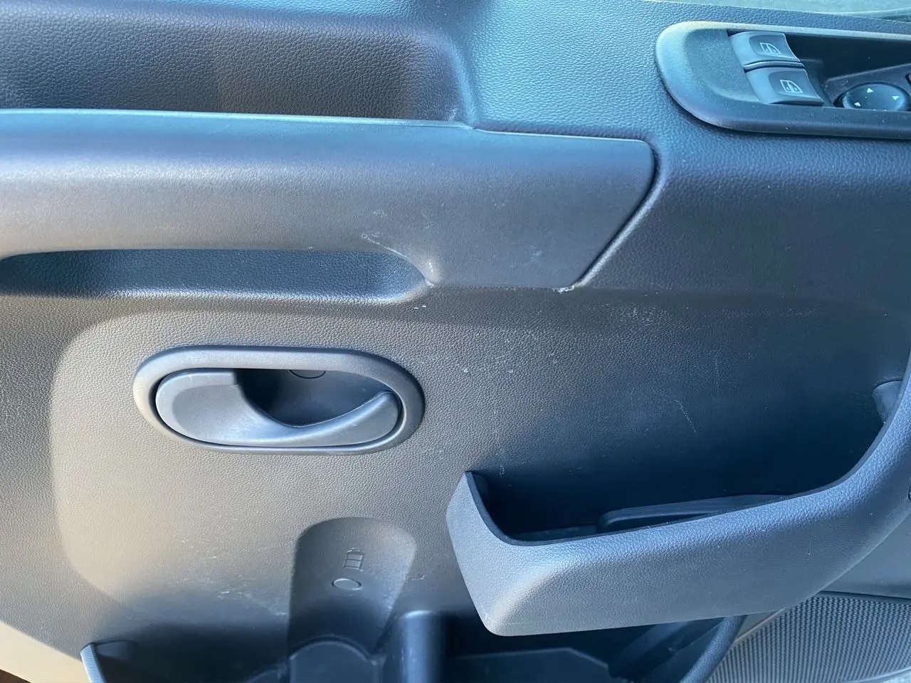 Gros plan sur la poignée intérieure et les commandes de fenêtre côté gauche d'un Nissan Interstar blanc.