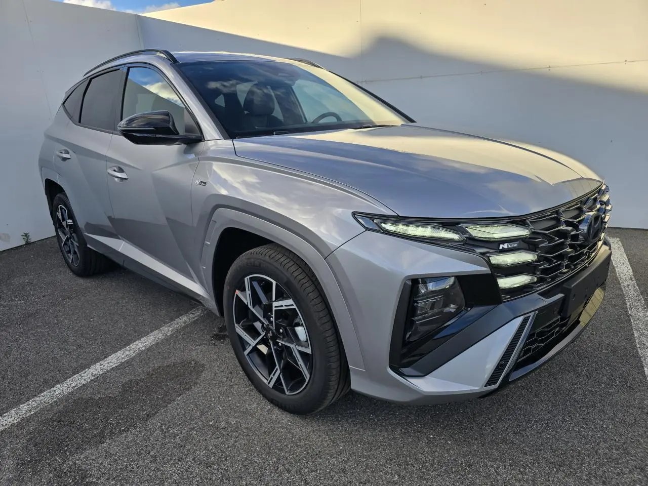 Hyundai Tucson 2025 gris argenté en vue 3/4 avant droit avec calandre N Line et jantes alliage noires.